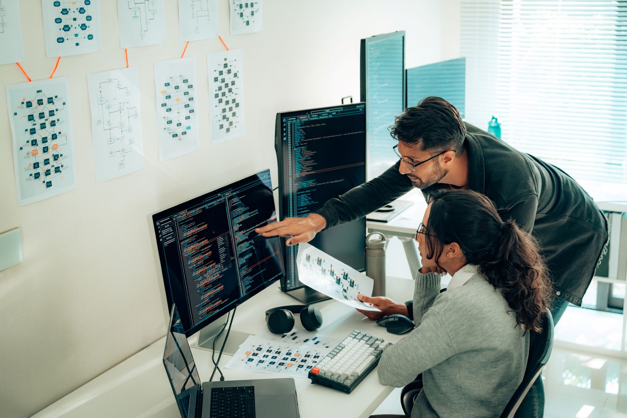 professor looking over the shoulders of and talking with a woman with code on her computer