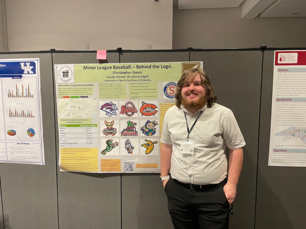 Reach Fellow at UNC Pembroke stands with his research presentation