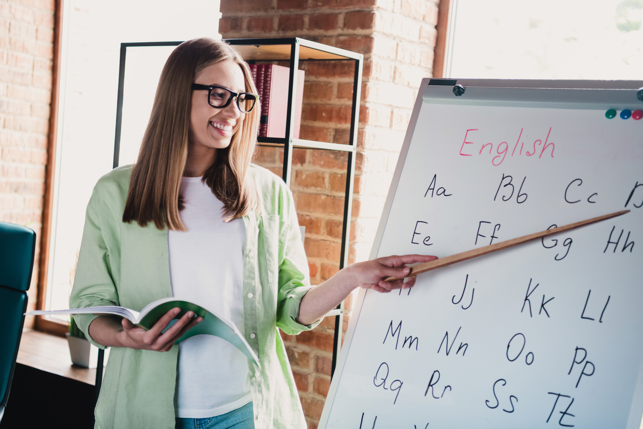 Woman pointing to a whiteboard with the english alphabet on it