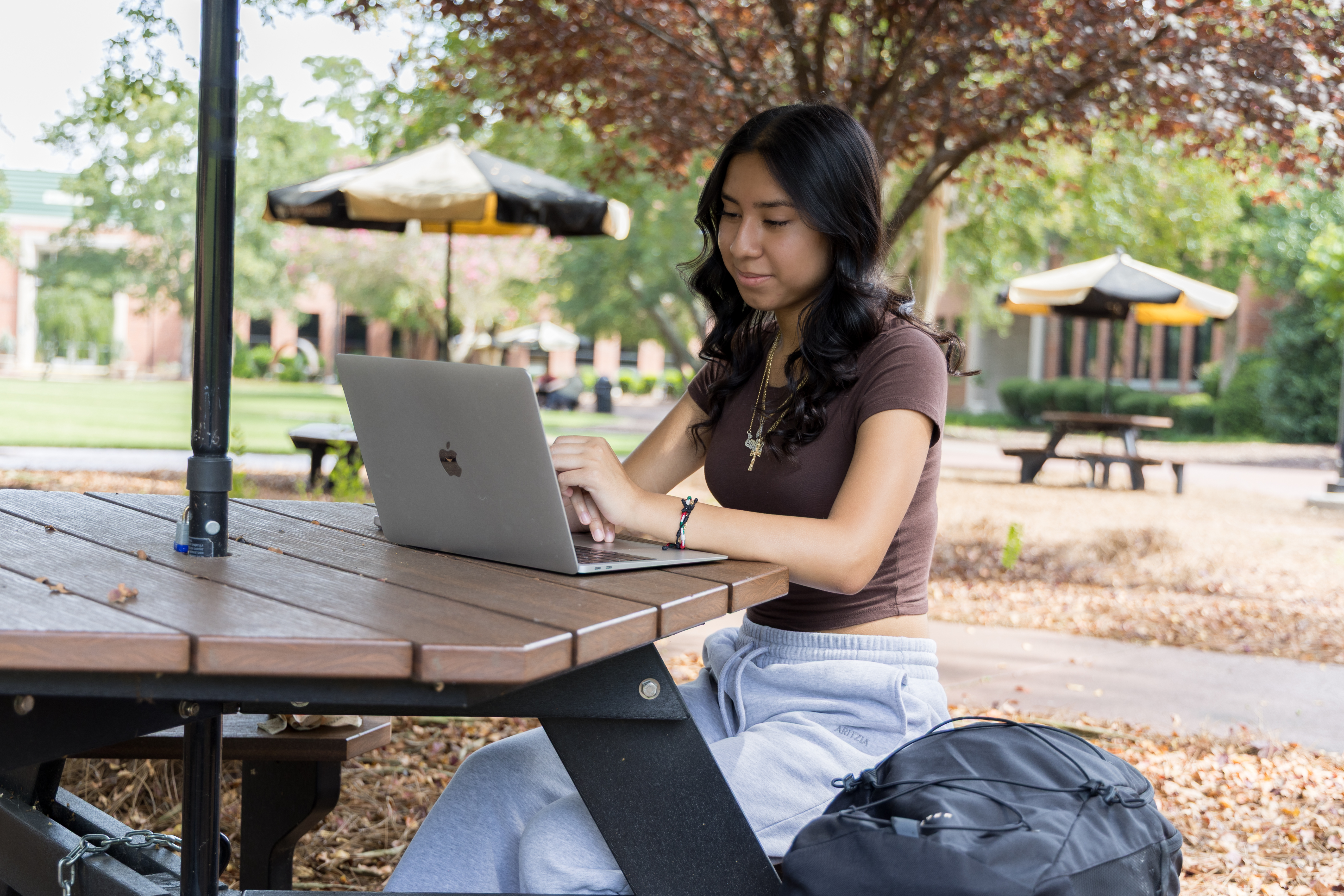 UNCP student studying on a laptop at a picnic table on campus.