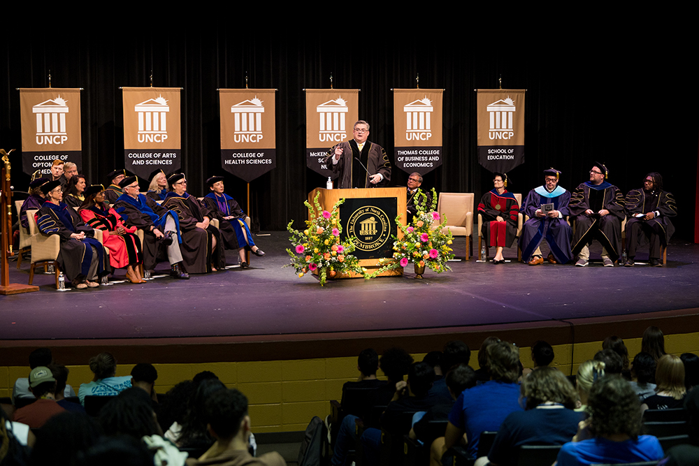 UNCP academic leadership dressed in regalia siting on a stage during convocation
