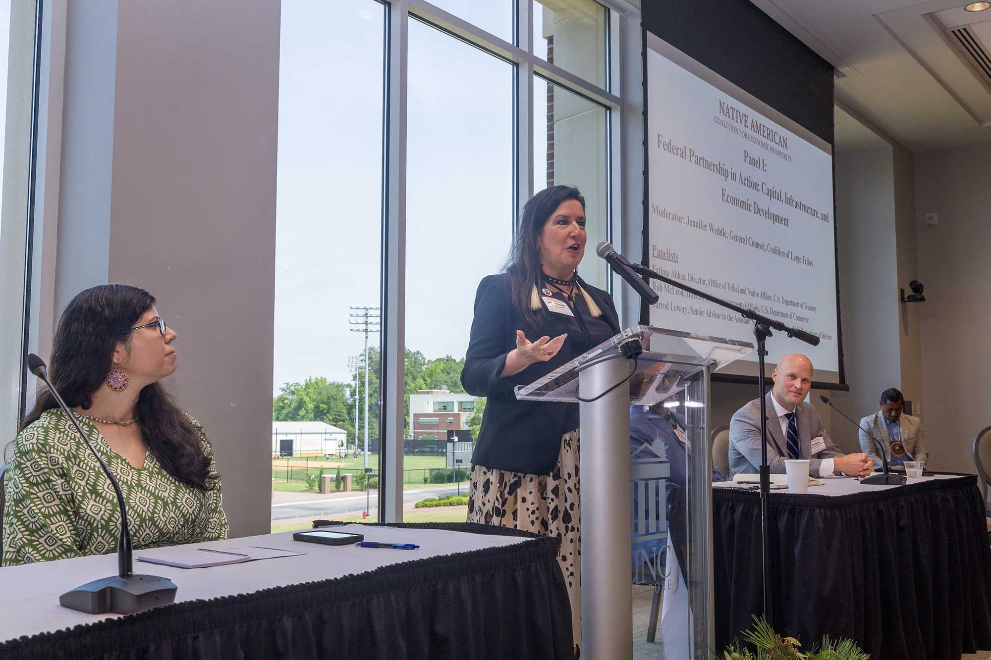 Panelists participate in a Native American Coalition for Economic Prosperity (NACEP) Government-to-Government Roundtable at UNC Pembroke, where a speaker addresses attendees during a discussion on federal partnerships, access to capital, infrastructure and economic development for tribal nations.