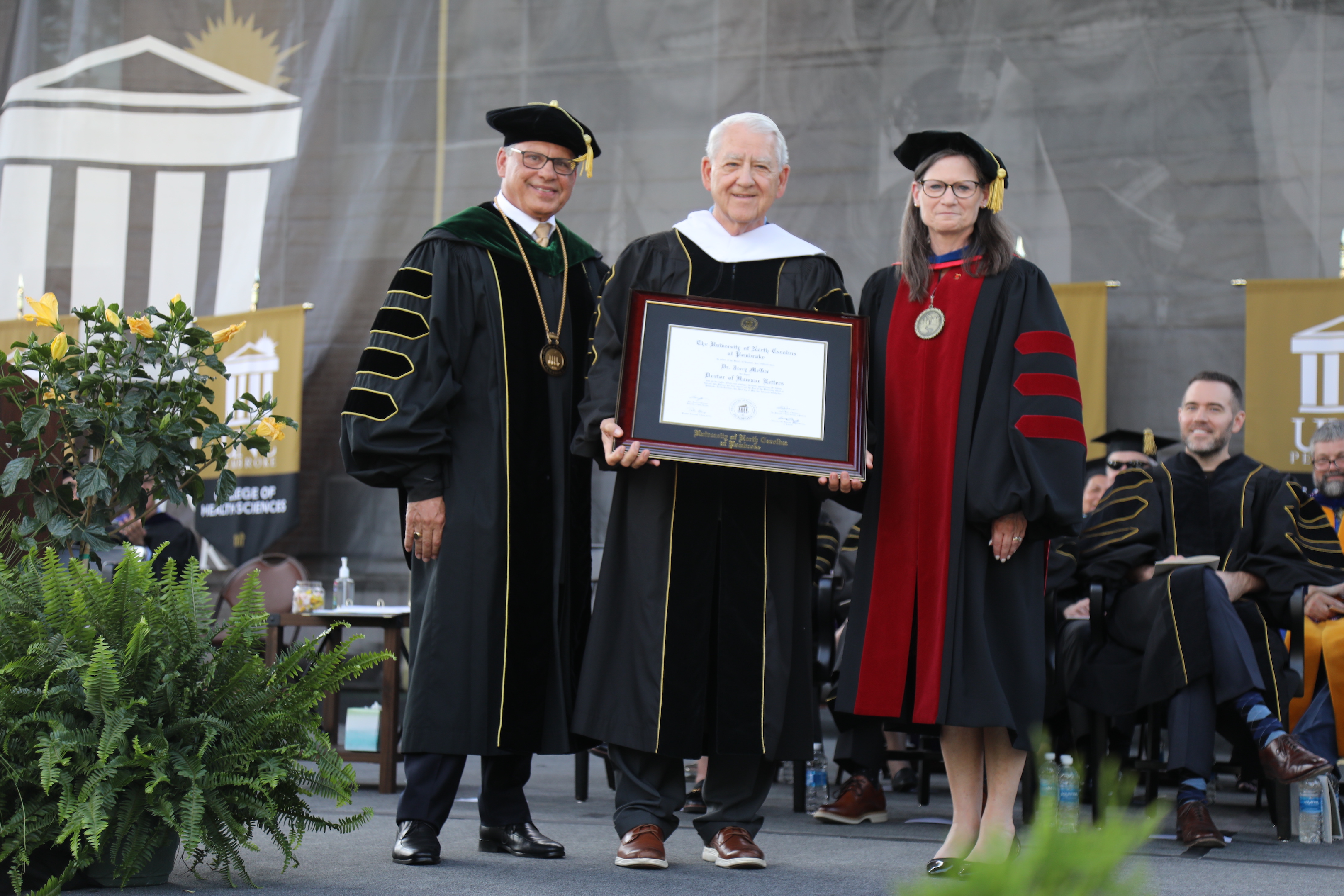 UNCP Chancellor Robin Cummings, honoree Jerry McGee, Provost Diane Prusank on stage at the UNCP commencement.