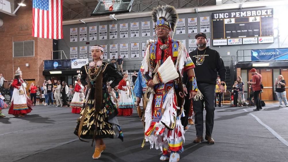 american indians in native garb walk across a court