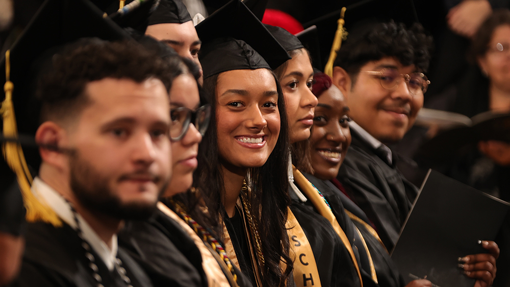 Students in regalia, including Sydney Brooks smiling at the camera, attend Winter Commencement