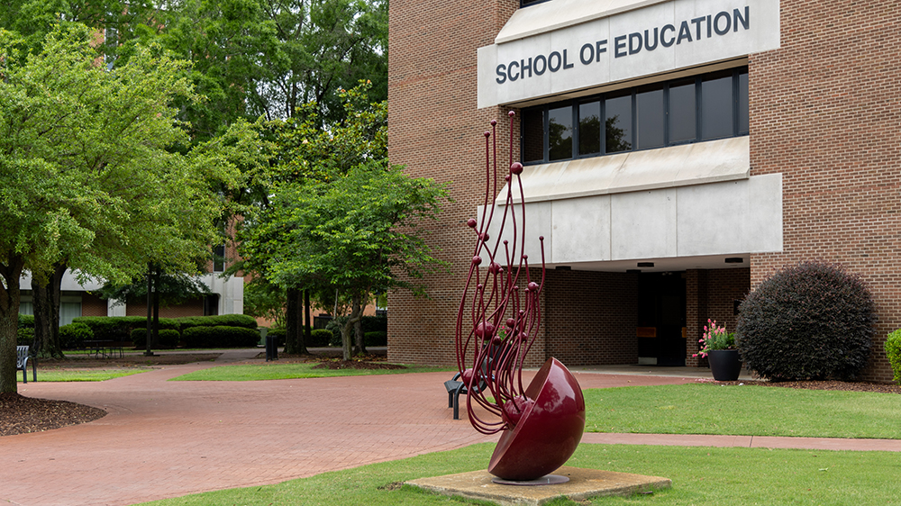 Exterior of UNC Pembroke’s School of Education building with trees and sculpture