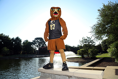 UNCP BraveHawk mascot standing at a water feature on campus
