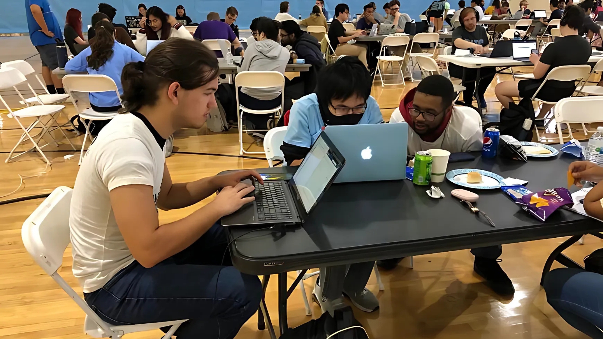 Students collaborate on laptops during a group activity or competition in a large indoor space filled with tables and chairs, showcasing student engagement and teamwork at UNC Pembroke.