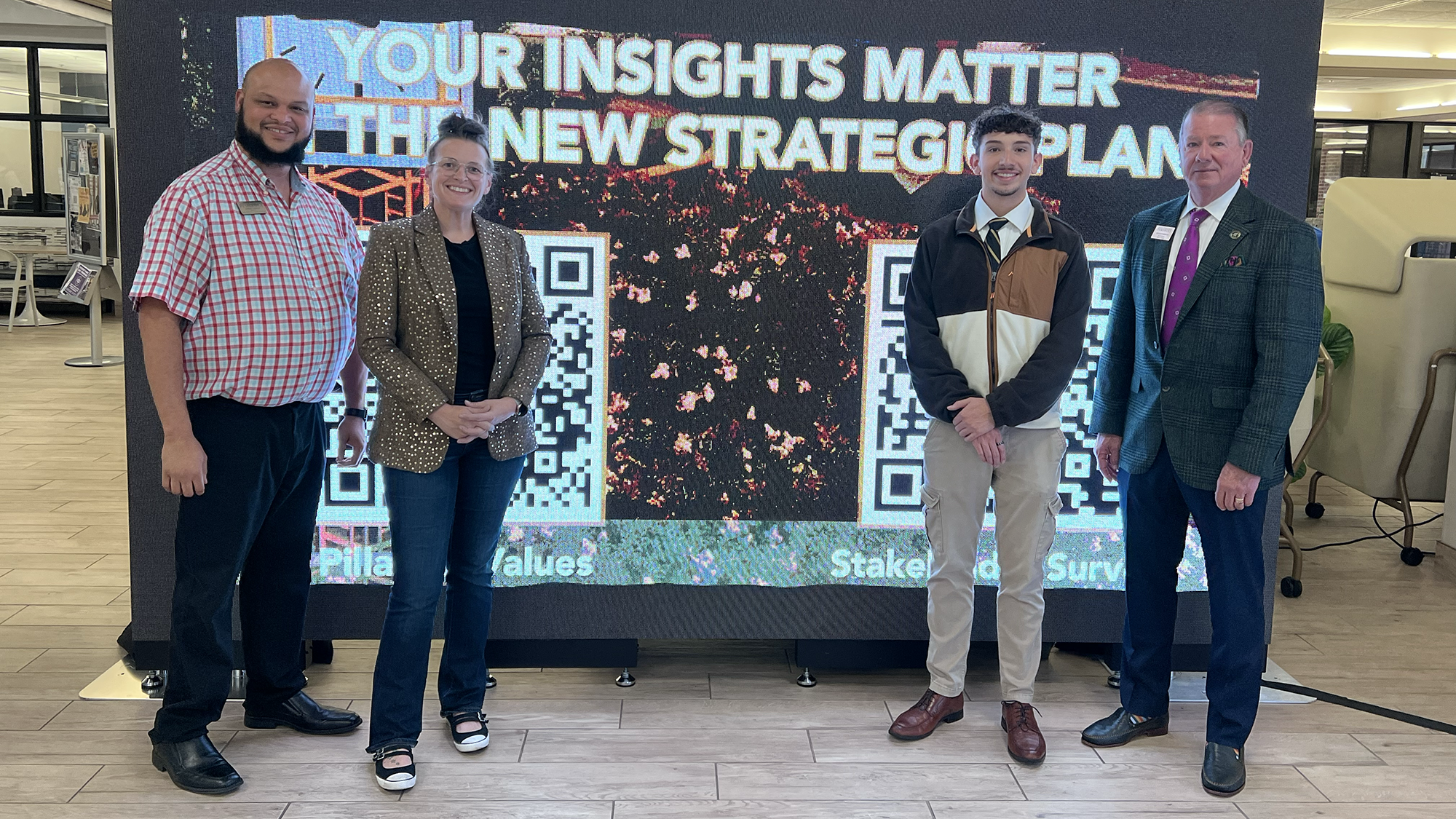 Members of the strategic planning committee stand in front of large screens during a campus event.