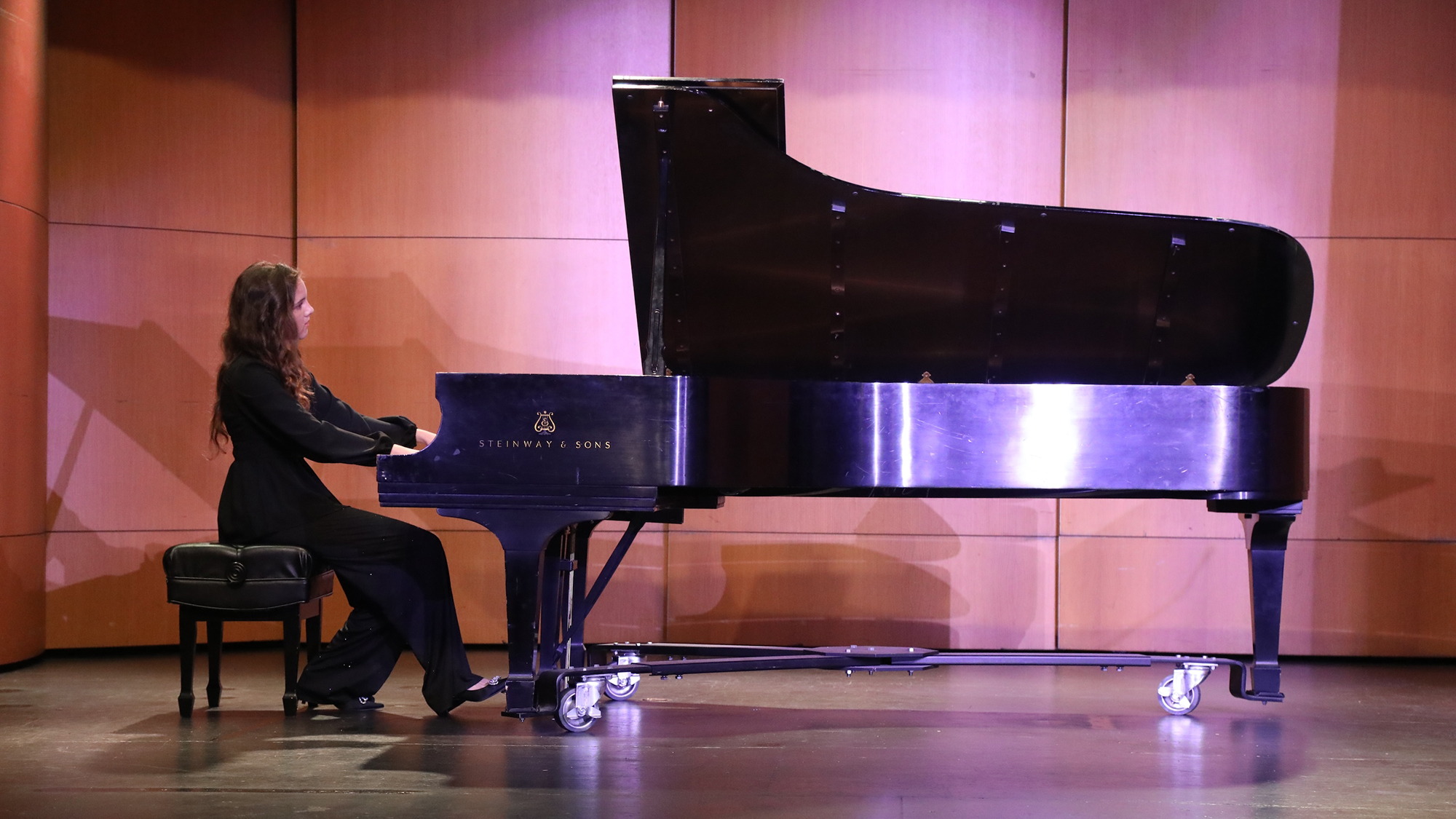 young female student playing a grand piano on stage