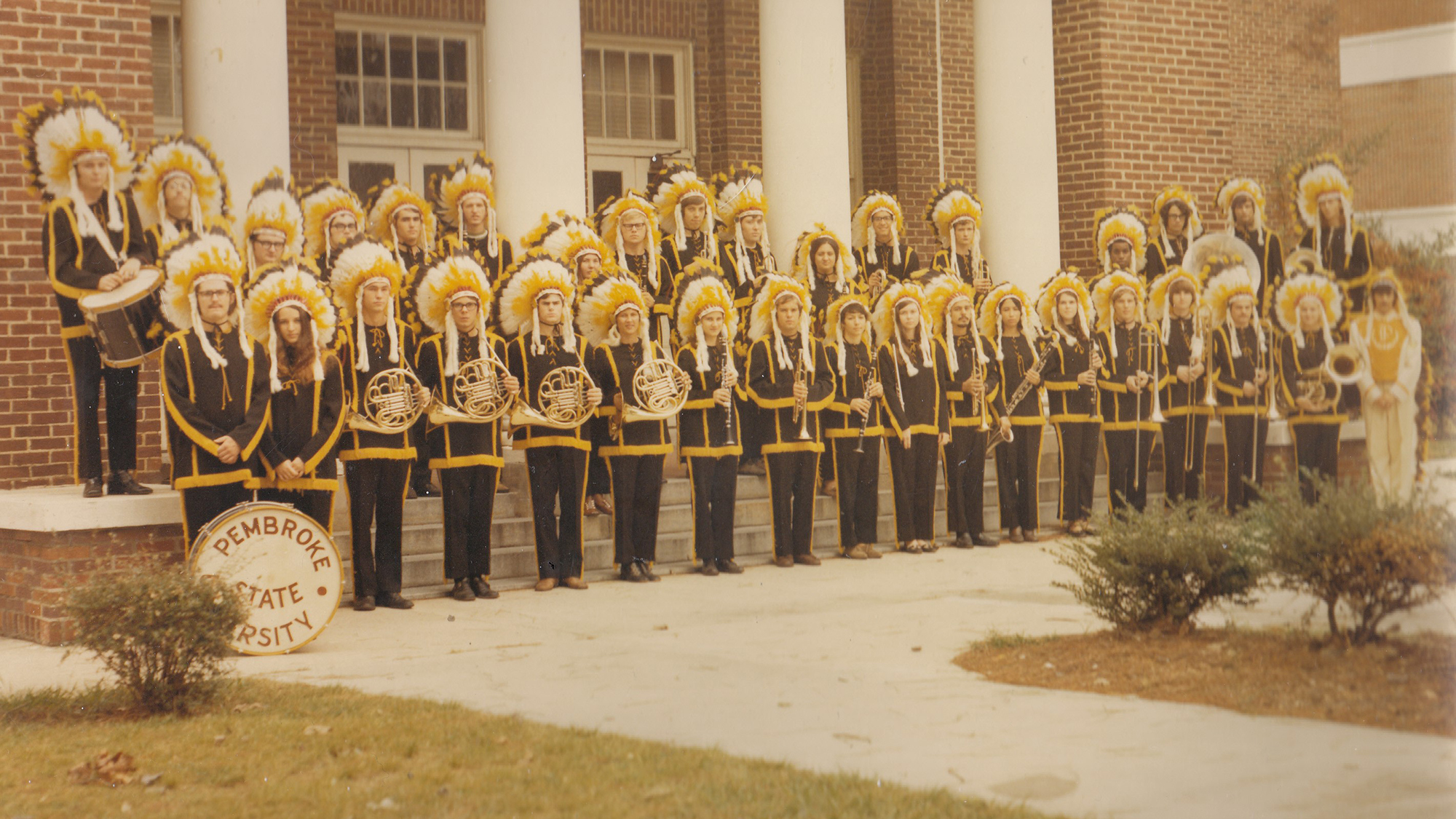 marching band posing in front of Old Main in full uniform including feathered headdresses