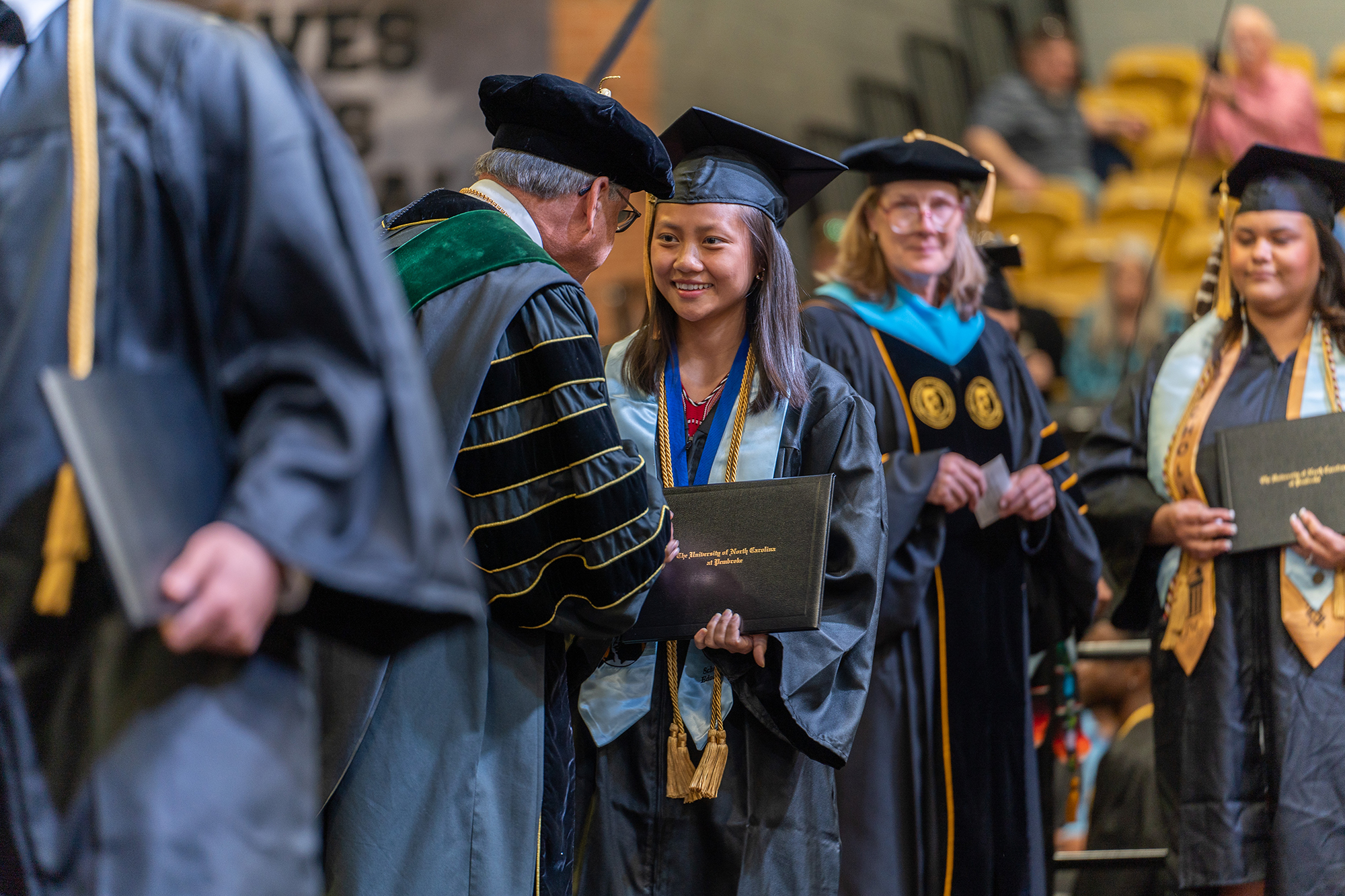 female UNCP student in regalia shaking the chancellor's hand