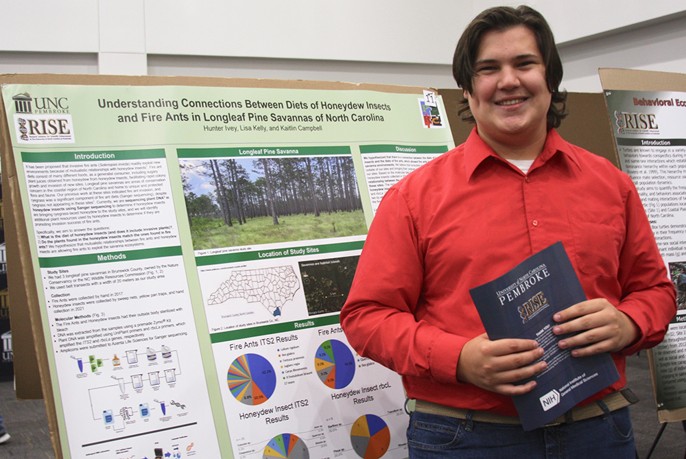 student stands in front of research poster at Compass Symposium