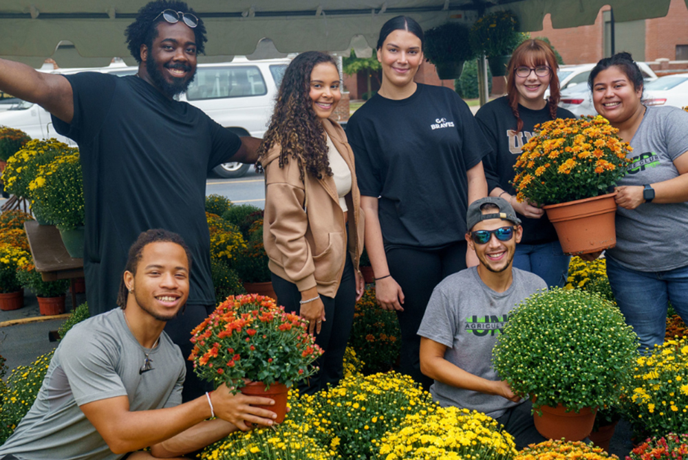 UNCP agriculture club students pose with potted plants at a campus plant sale