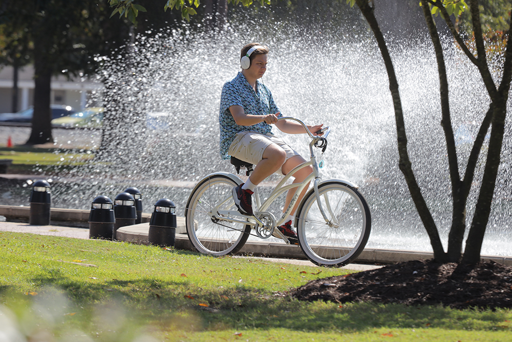 male on campus by water feature on bike UNCP
