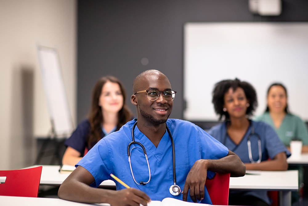 nursing student sitting in class with a smile on his face giving the apperance he is engaged with whats going on.