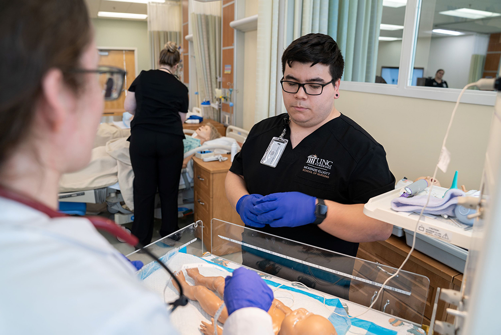 Male graduate student in nursing at UNC Pembroke in a newborn simulation lab working on a robotic newborn baby simulation man·ne·quin.