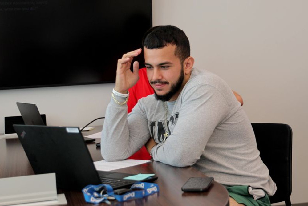 Male UNCP student smiling while looking at his laptop in a classroom.