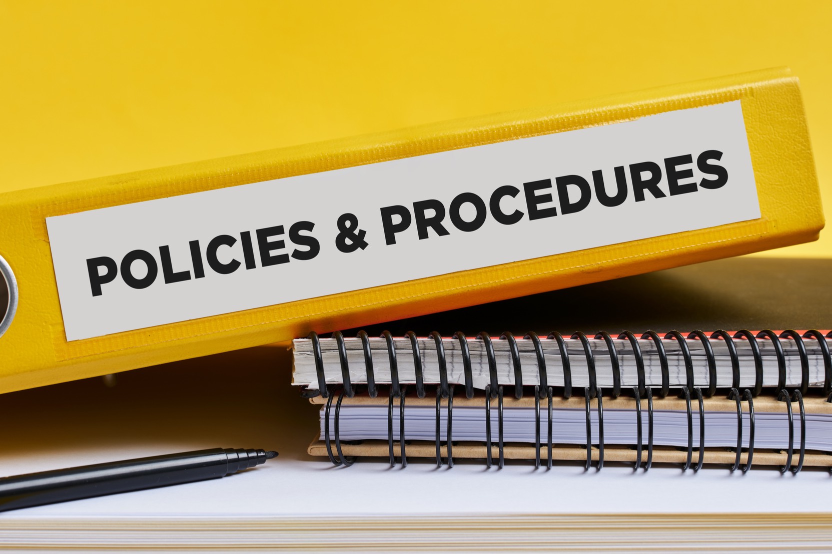 A short stack of notebooks and binders. The top binder has a label, "Policies and Procedures" on the spine.