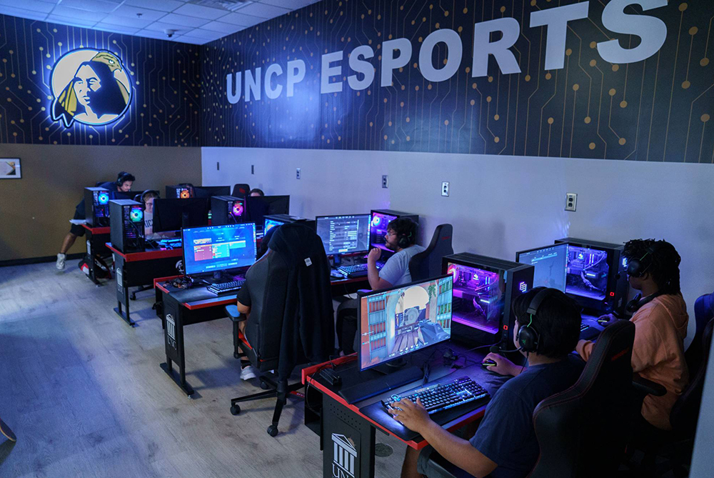 UNCP Esports facility, room with multiple gaming PC's and a glowing university logo on the wall