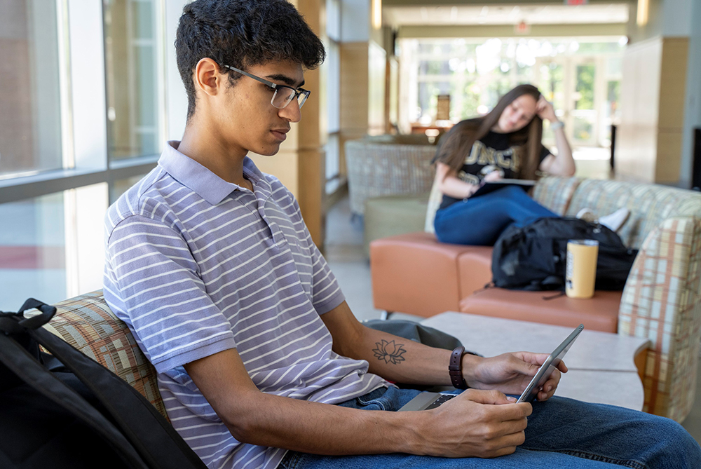 Male UNC Pembroke student in a lounge area on a tablet with a keyboard.