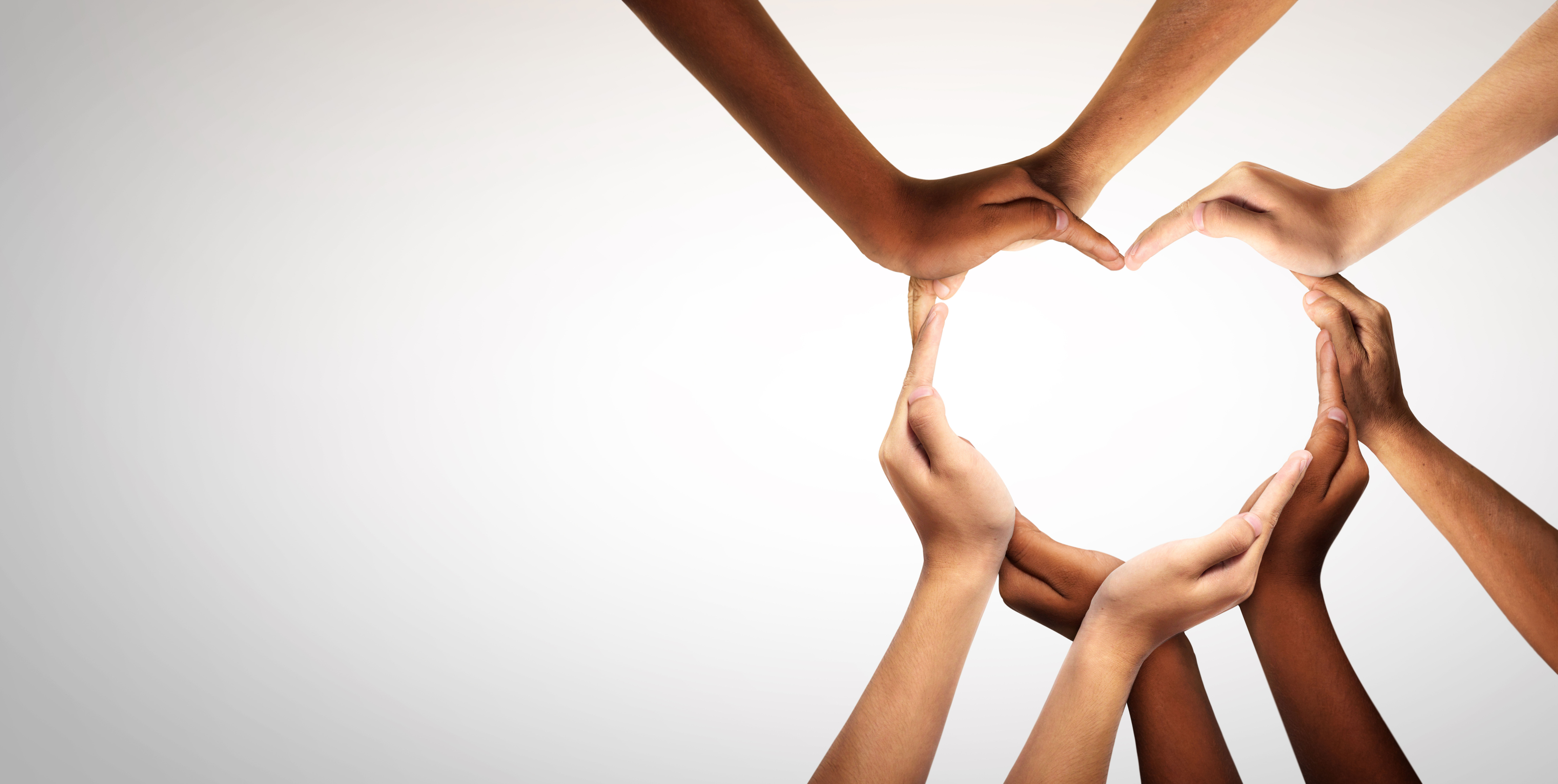 White backdrop with hands reaching in from out of frame coming together to form a heart with the shape of their fingers.