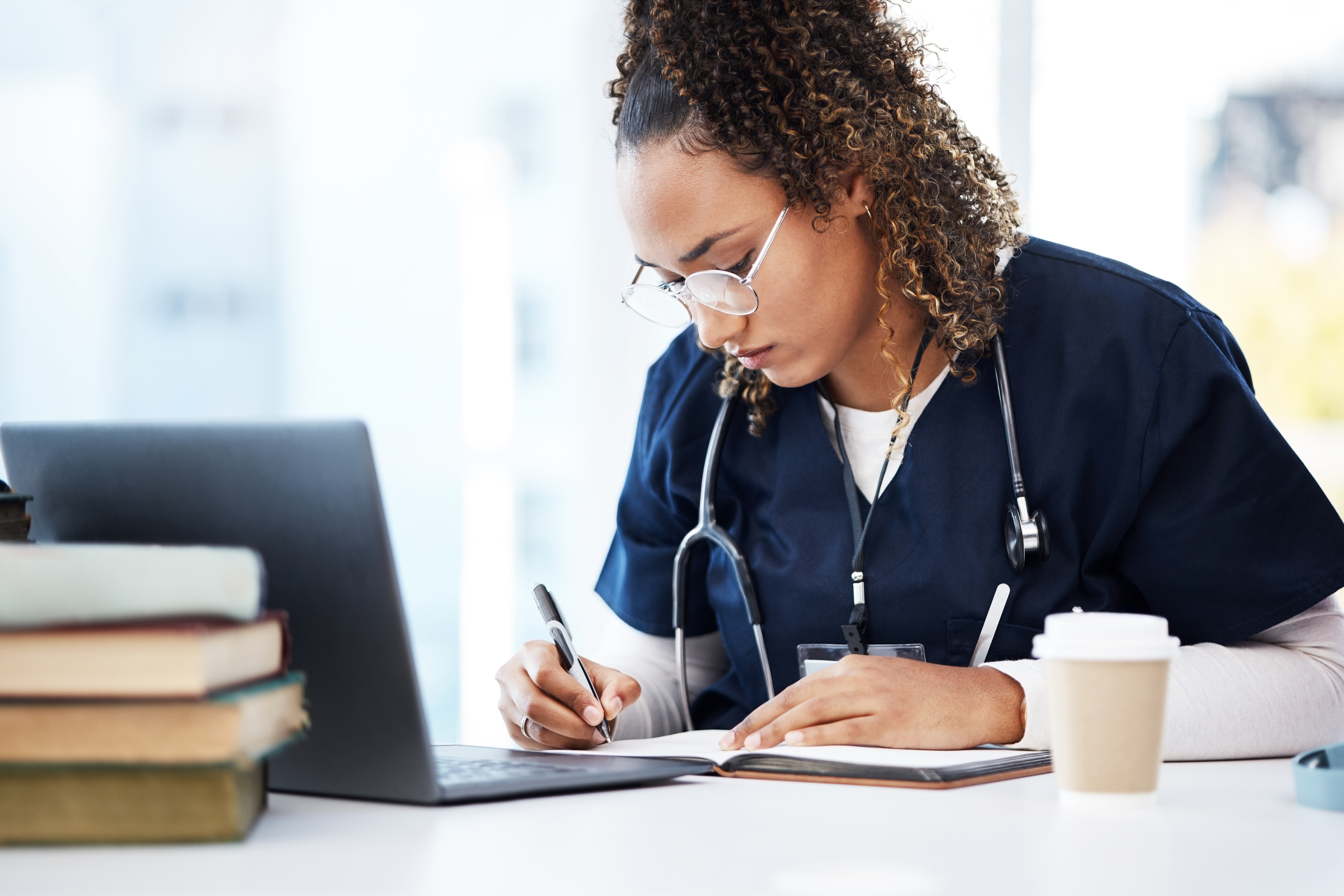nurse with glasses looking down at laptop while surrounded by notebook as if shes studying