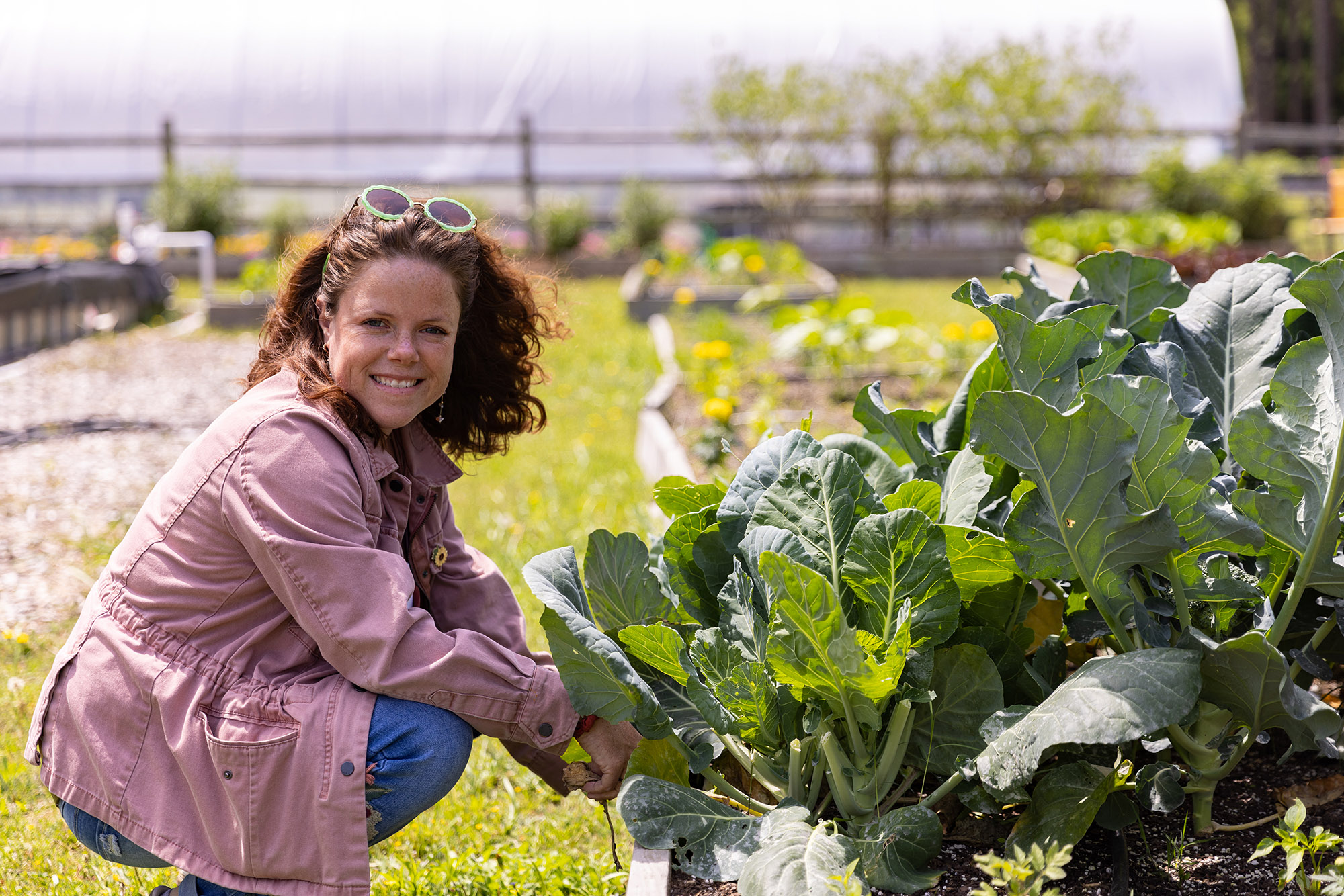female agriculture student crouched down beside a row of green vegetables in a garden