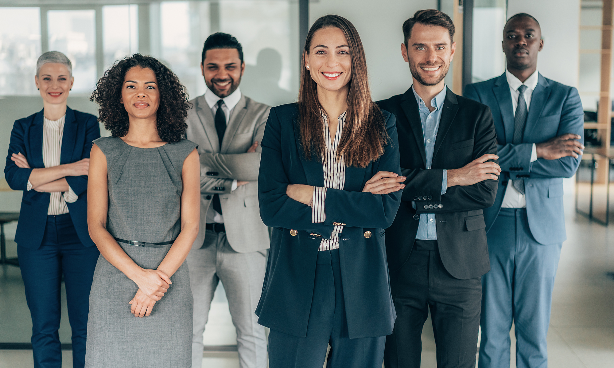 Group of diverse business professionals in formal attire standing confidently in an office setting, symbolizing leadership and teamwork.