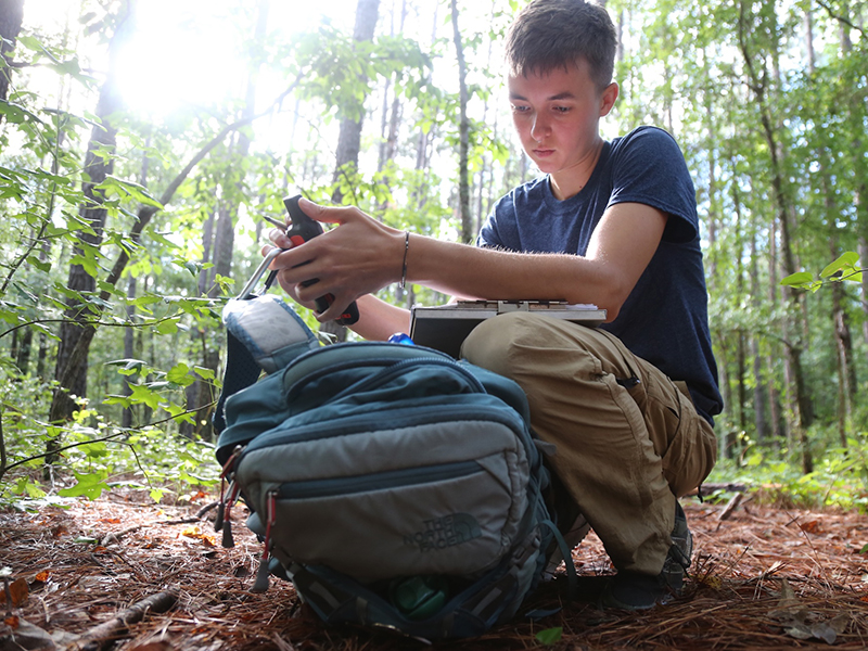 A UNCP agriculture student collects data in a wooded field site, representing environmental and natural resource career pathways.