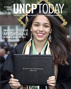 graduate holding a diploma folder from the cover of the UNCP Today spring 2018 edition