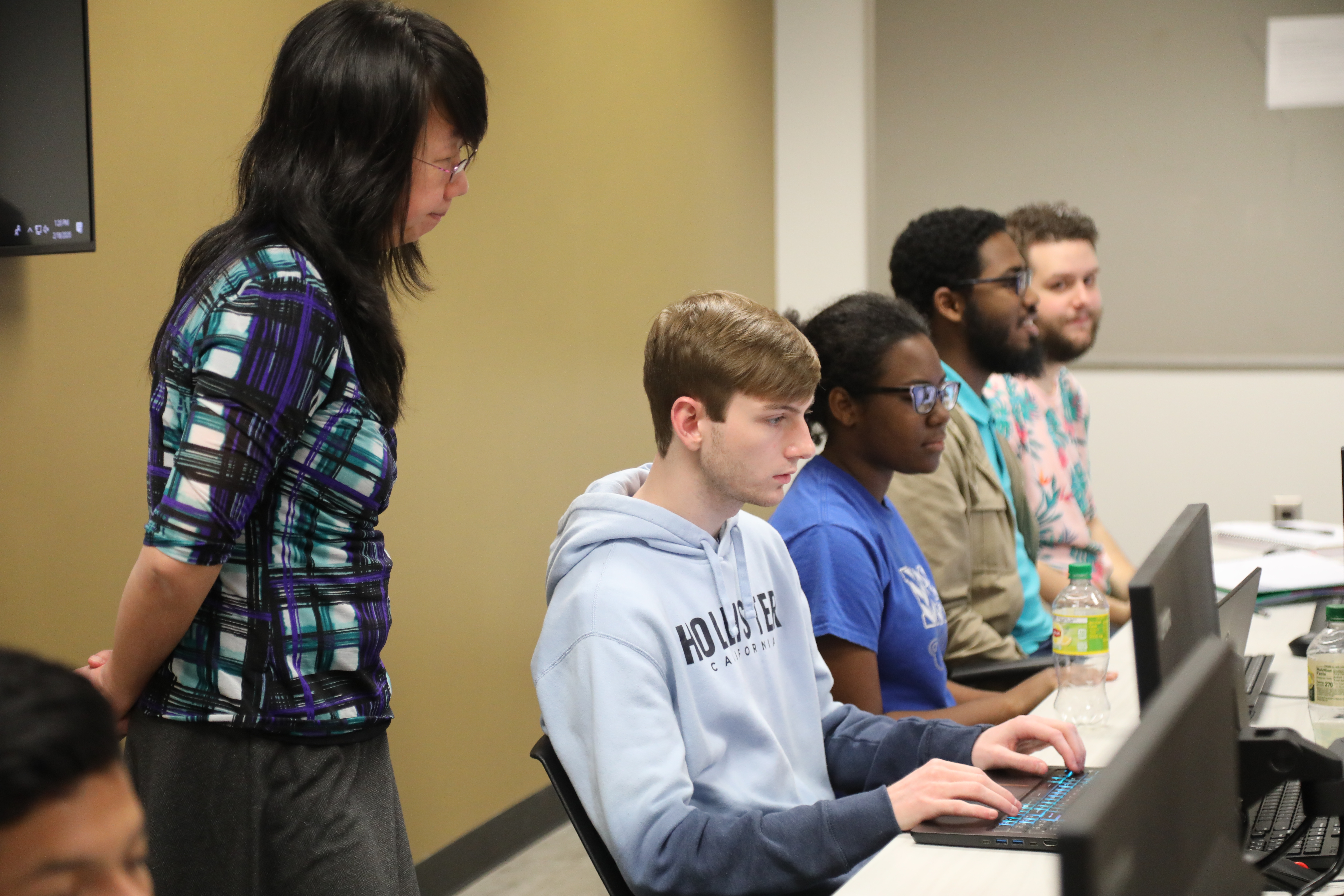 professor looks over the shoulder of students in cybersecurity classroom at UNCP