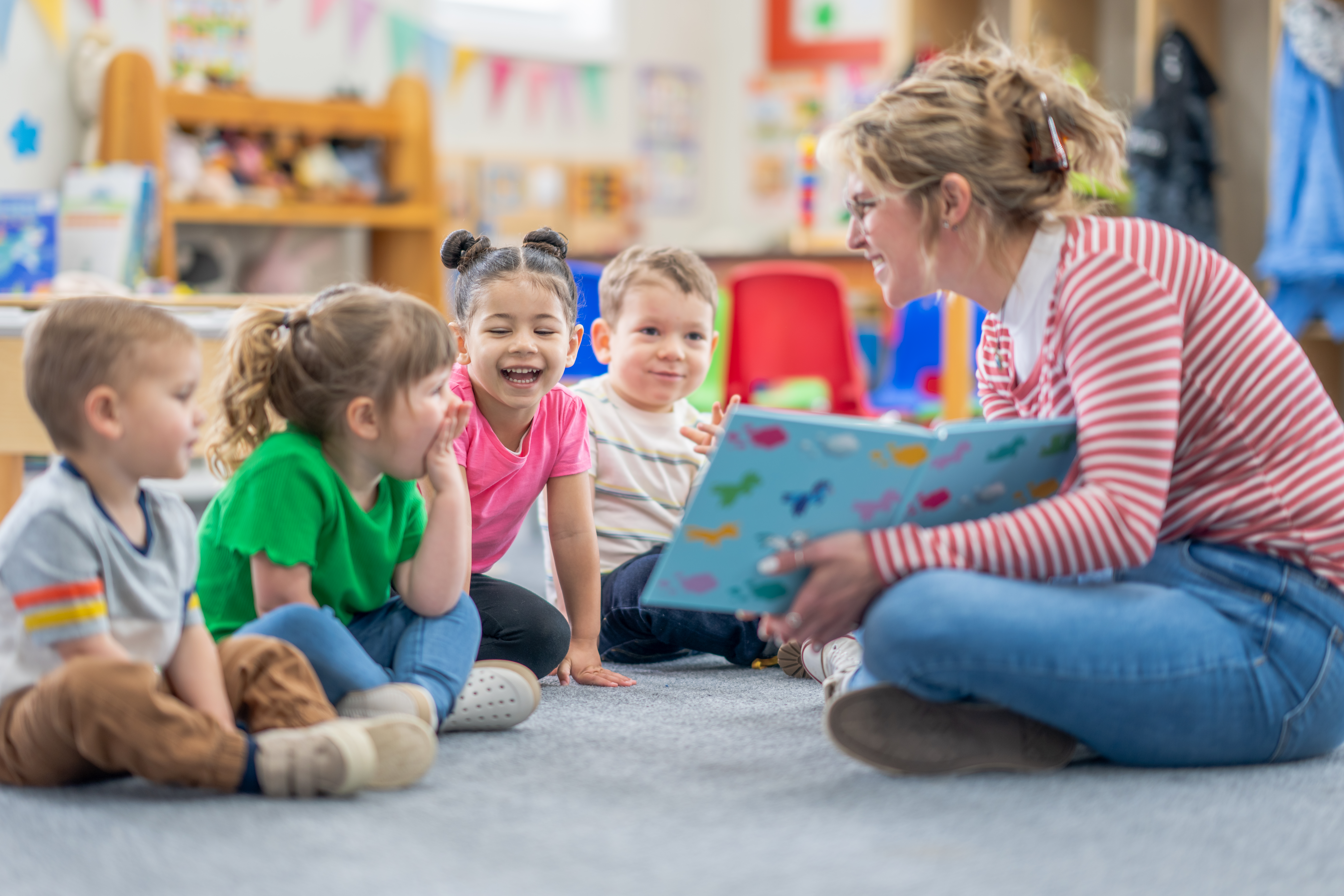 female teacher sitting on the floor reading to children
