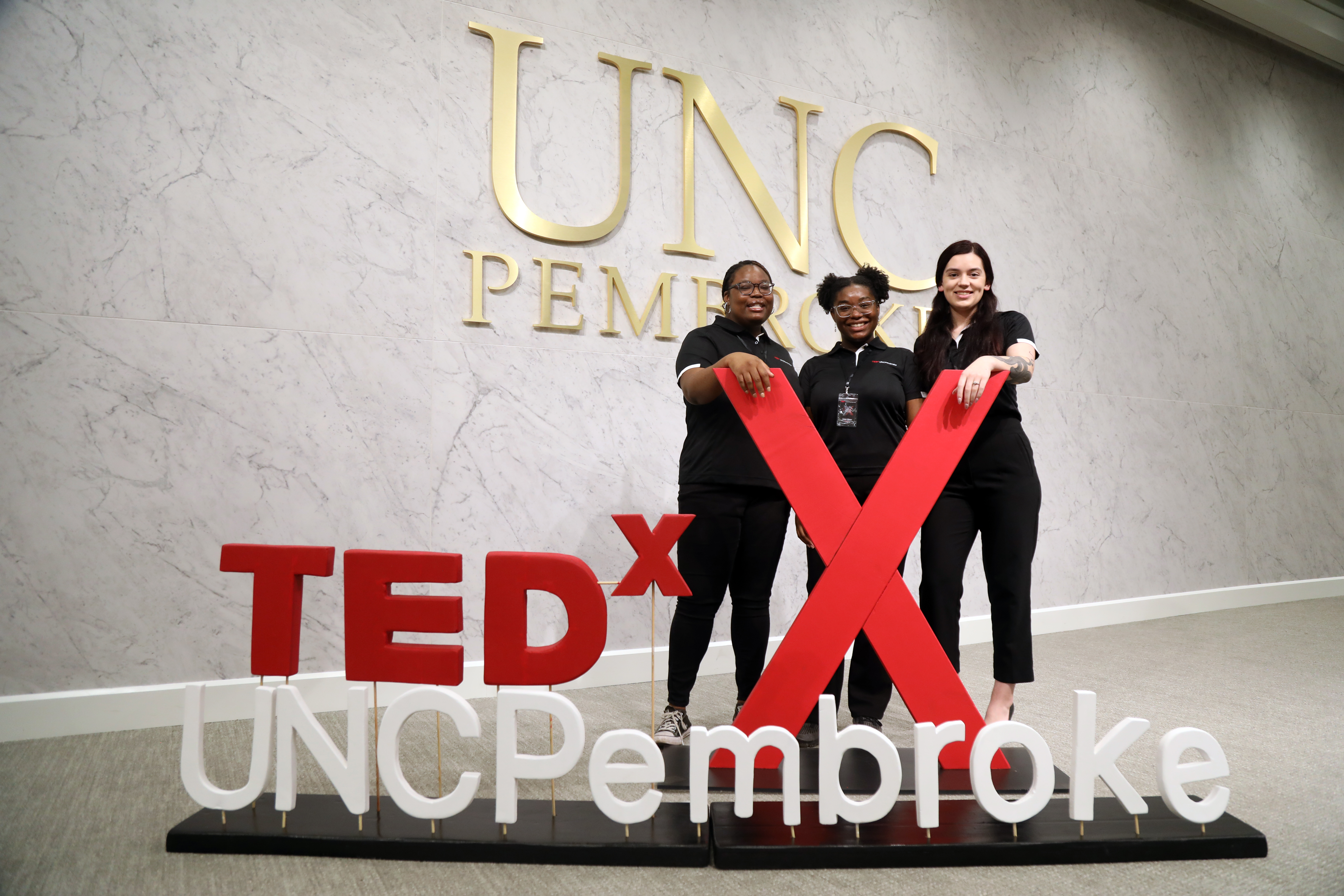 Three female students in front of a TEDX sign at UNC Pembroke.